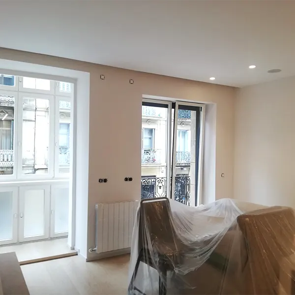 Salón de un piso en reforma con las paredes pintadas de blanco y con balcón.